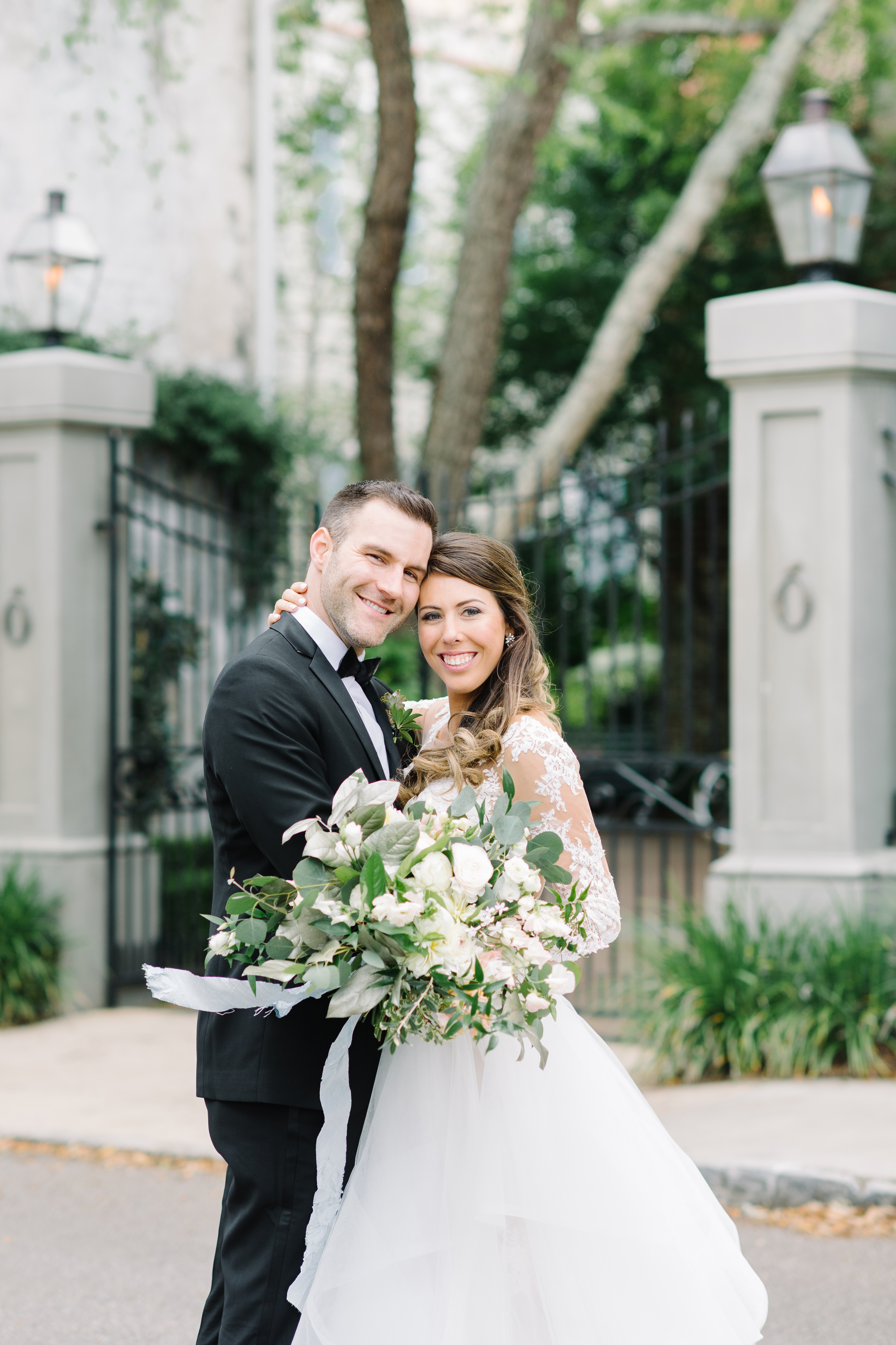 Bride and groom in front of a wrought iron gate in downtown Charleston. Black tie wedding. Wedding gown with lace sleeves